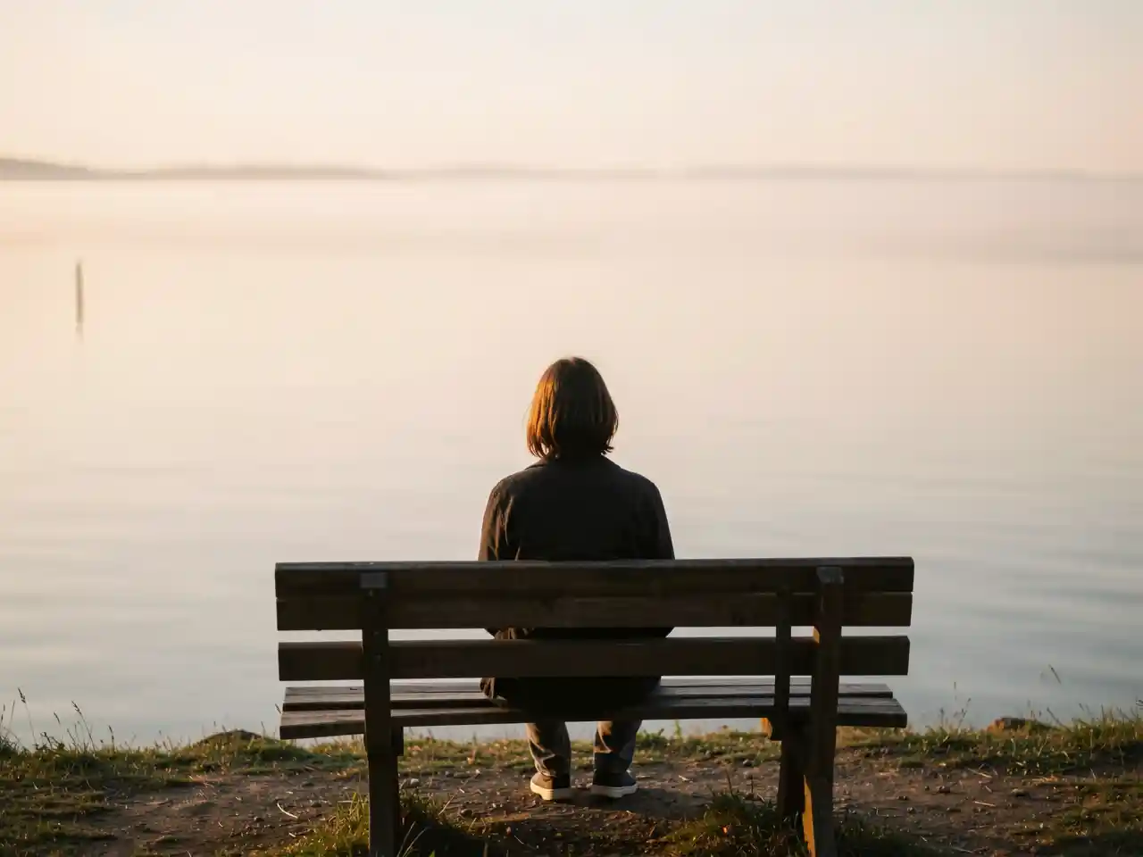 A person sitting alone on a bench overlooking a calm lake at sunset, symbolizing quiet reflection, inner peace, and the journey of self-discovery