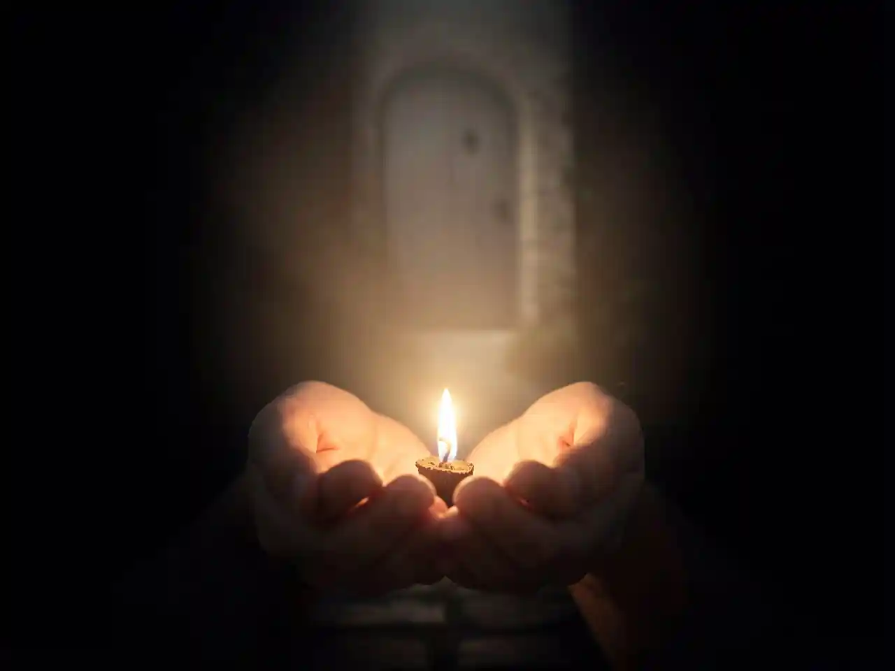 Cupped human hands gently holding a single, tiny glowing flame, whose light softly expands to illuminate a faint path in the surrounding darkness, symbolizing the quiet power of a willing heart and the divine multiplication of even the smallest faith