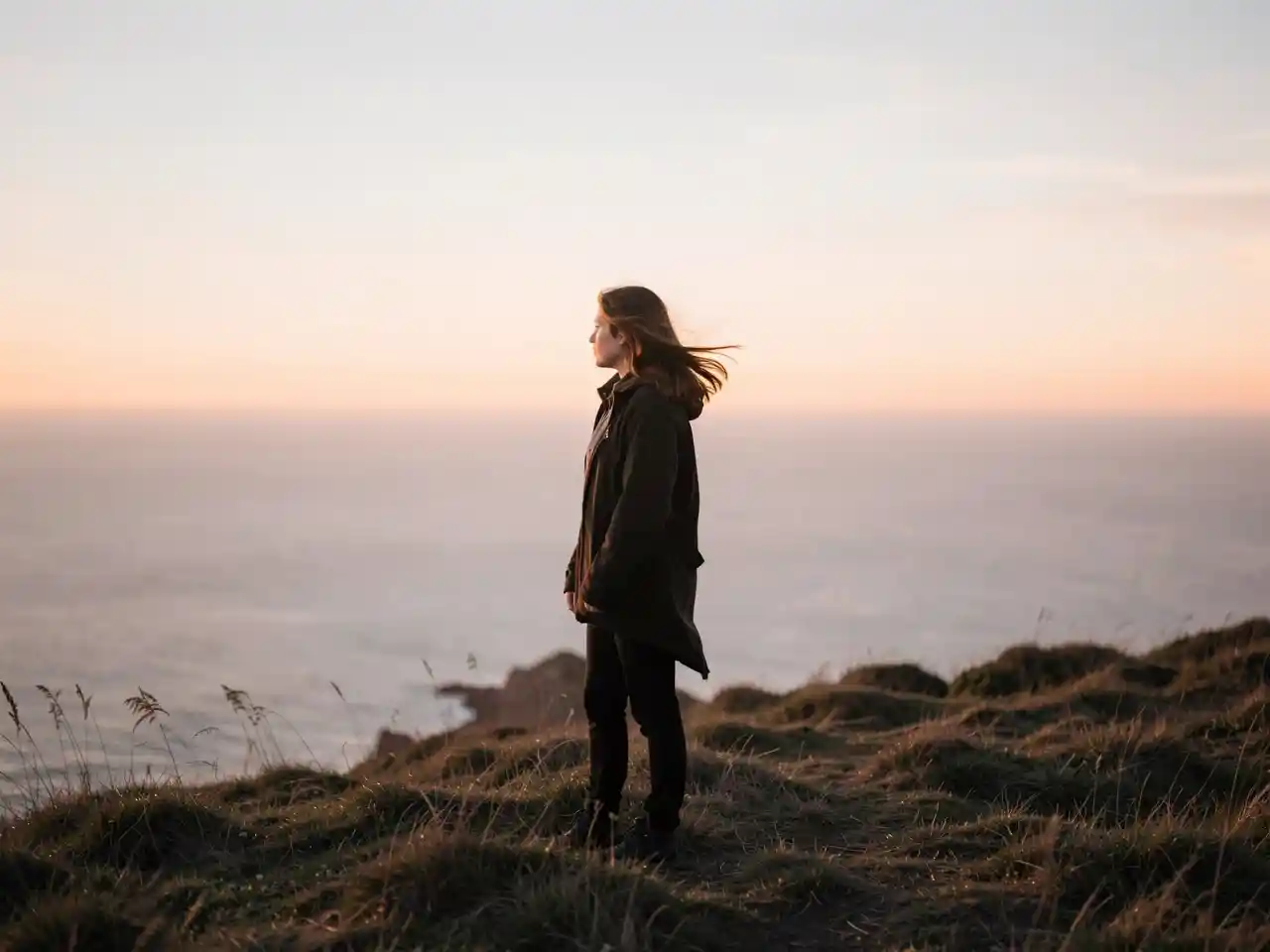 Lone figure standing on a windswept hill at dusk, contemplating in the quiet light