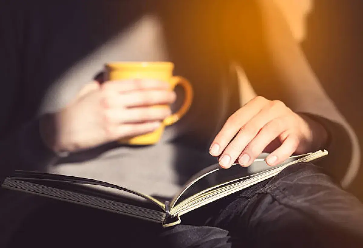 Hands holding a journal and tea cup, symbolizing reflection and mindful presence