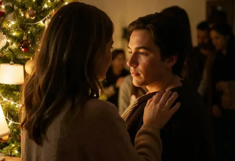 A mother gently touching her adult child's shoulder by a warm Christmas tree, symbolizing the shelter of home and the enduring strength of love.