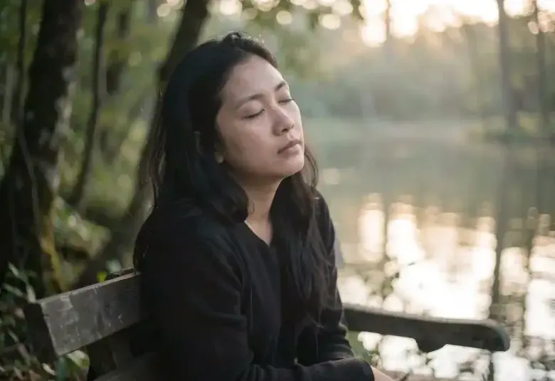 A person sitting in quiet contemplation in nature, symbolizing the spiritual practice of listening with the heart and finding abundance in presence.