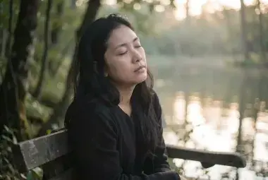 A person sitting in quiet contemplation in nature, symbolizing the spiritual practice of listening with the heart and finding abundance in presence.