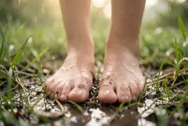 Close-up of bare feet standing on rain-dampened earth with soft, blurred greenery in the background, symbolizing the quiet joy and presence found in tiny, sacred escapes