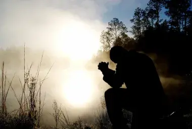A silhouette of a person kneeling in prayer at dawn's light